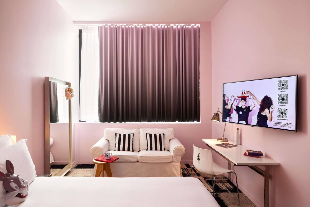 Een hotelkamer met een bed, een witte bank, een bureau, een televisie en een raam met gordijnen.