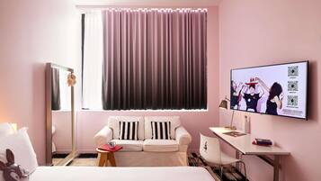 A hotel room with a bed, a white sofa, a desk, a television, and a window with curtains.