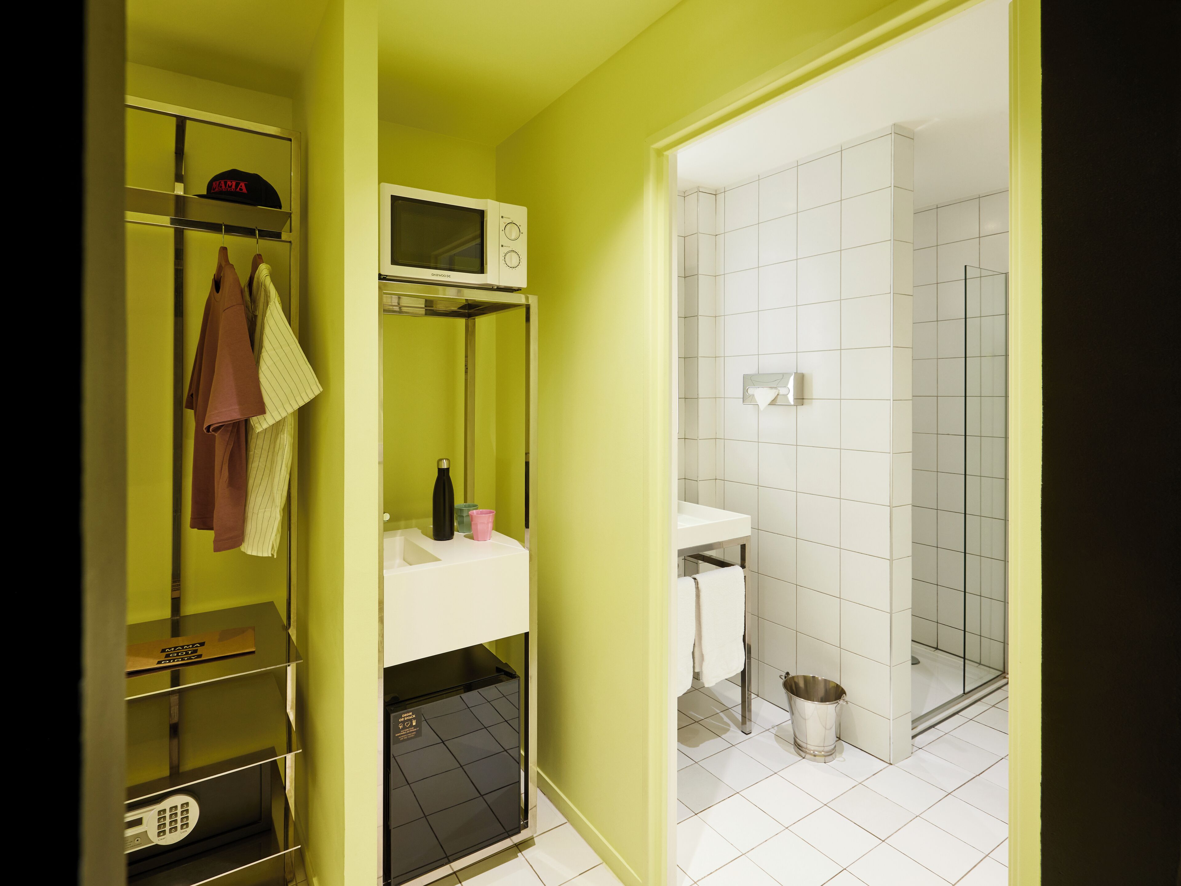 Une salle de bain avec un lavabo blanc, des toilettes et un espace douche. On y trouve une étagère avec un four à micro-ondes et une bouteille.
