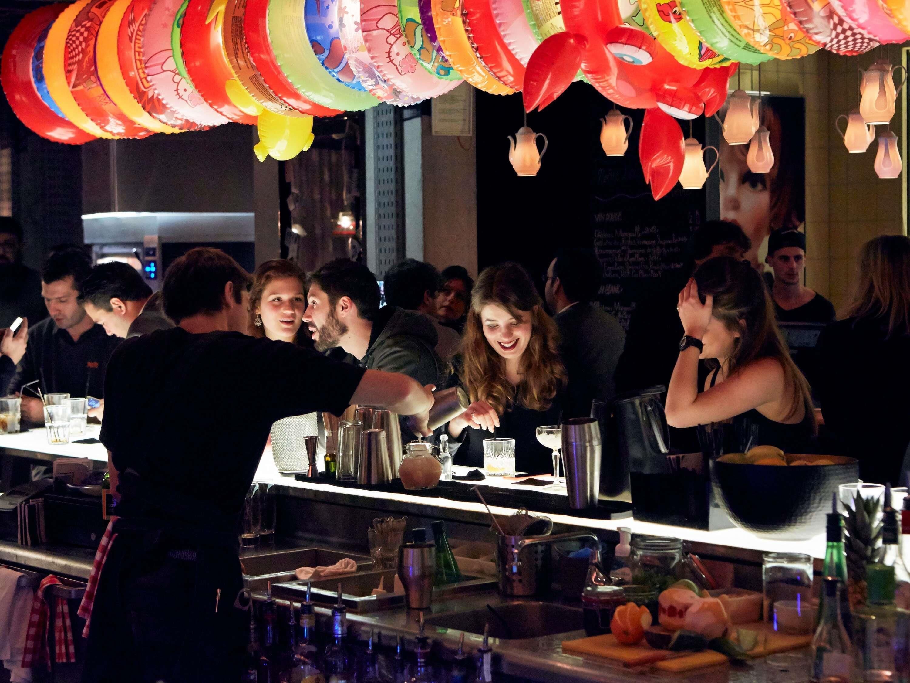 Eine Bar mit einem Barkeeper, einer Theke mit verschiedenen Flaschen, Gläsern und einer Speisekarte im Hintergrund.
