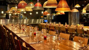 Un restaurante con varias mesas dispuestas, copas de vino y velas, y lámparas colgantes de colores.