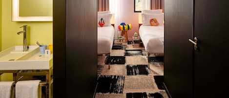 Hotellihuone, jossa on peilillä päällystetty seinä, pesuallas, sängyssä tyyny ja ruutukuviollinen matto.