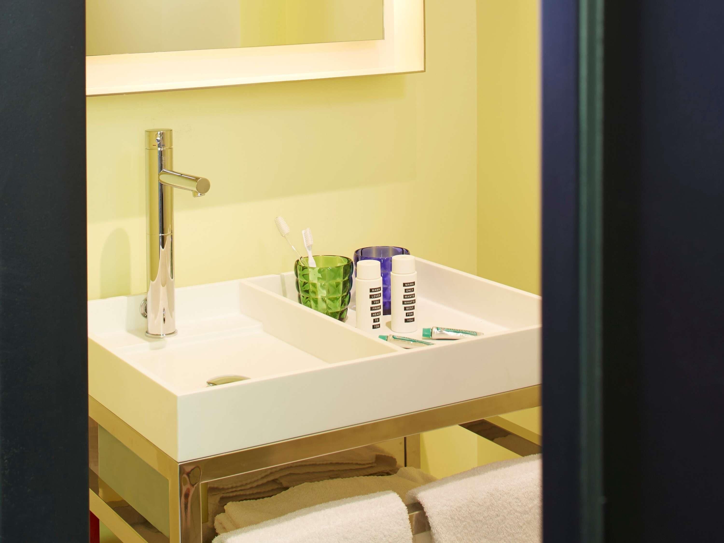 A bathroom with a white sink, a mirror above it, and a green glass container holding toothbrushes.