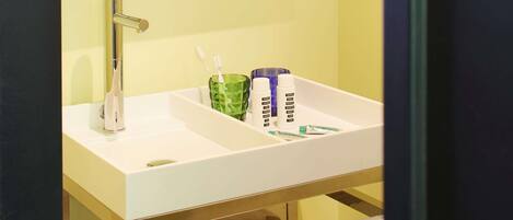 A bathroom with a white sink, a mirror above it, and a green glass container holding toothbrushes.