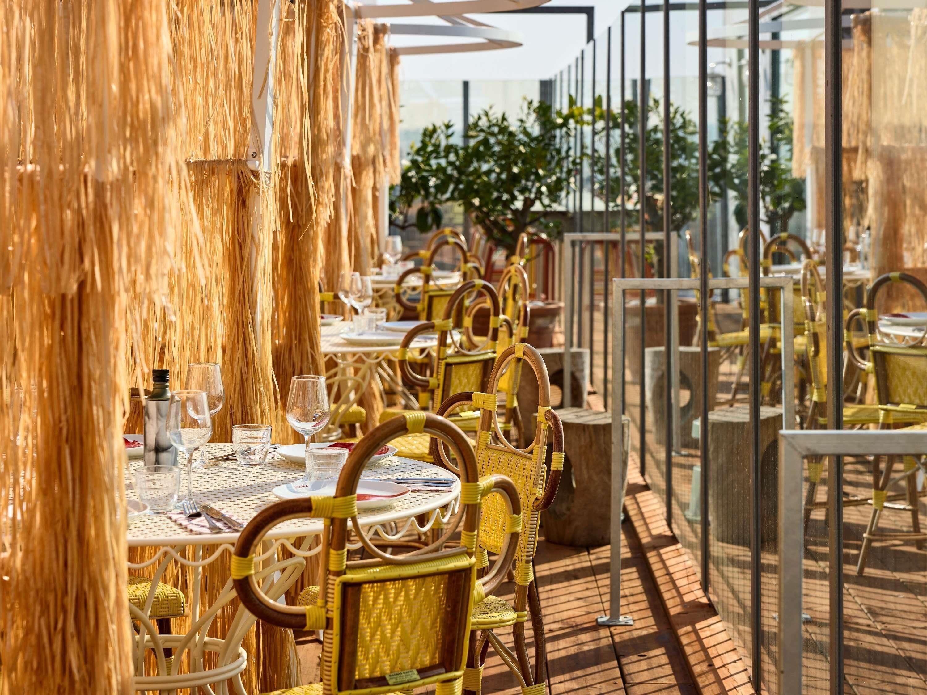Tables et chaises pour les repas en plein air, une rambarde en verre et une vue sur le ciel.