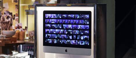 A computer monitor displaying a video with multiple scenes, mounted on a wall in a room with a bar area and stools.