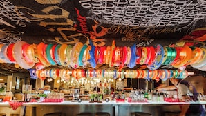Zona de bar con taburetes, una barra y un techo decorado con adornos colgantes de colores.
