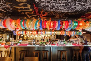 Een bar met krukken, een toonbank en een plafond versierd met kleurrijke hangdecoraties.