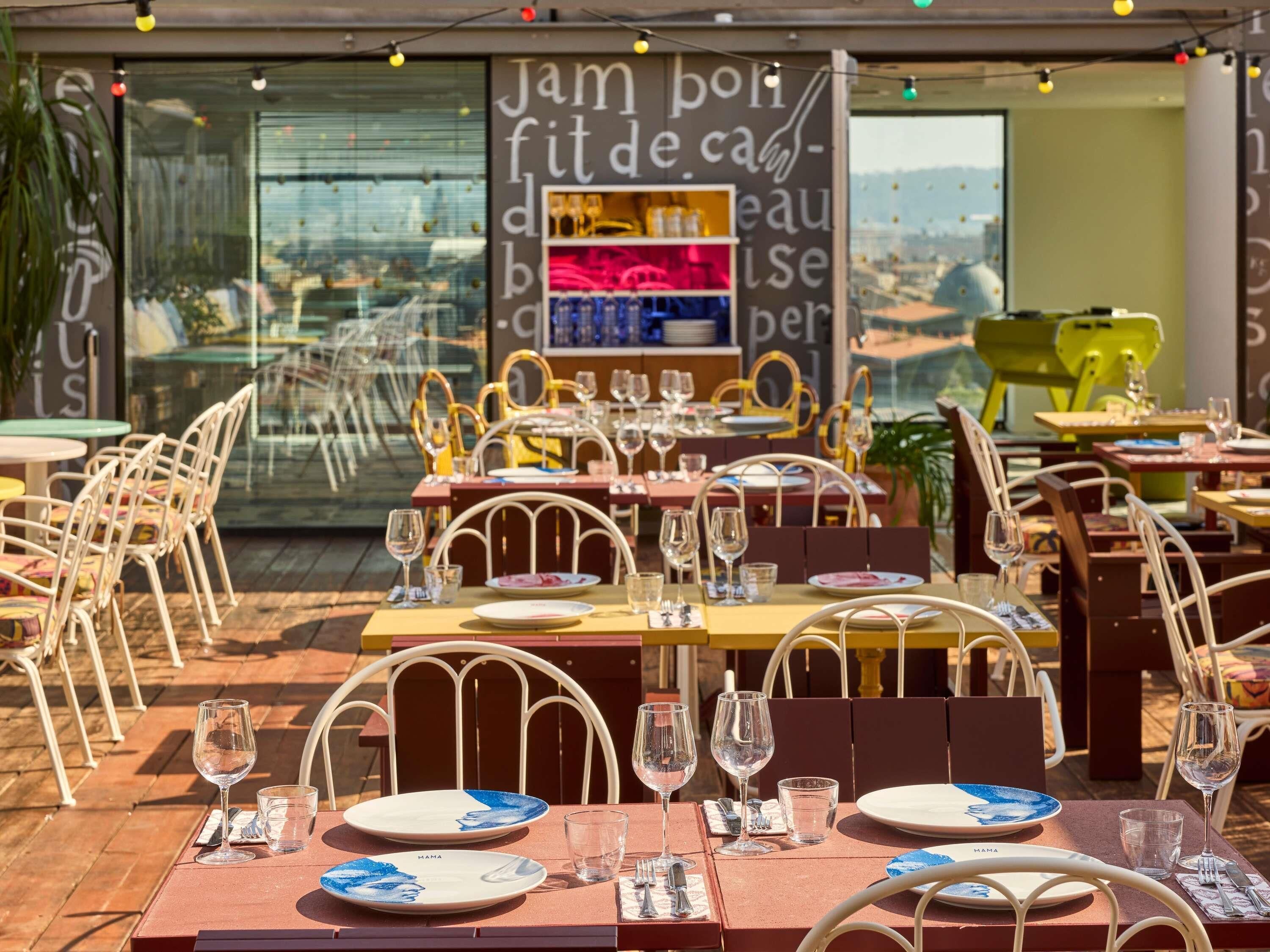 An outdoor dining area with tables set for two, chairs, and wine glasses.