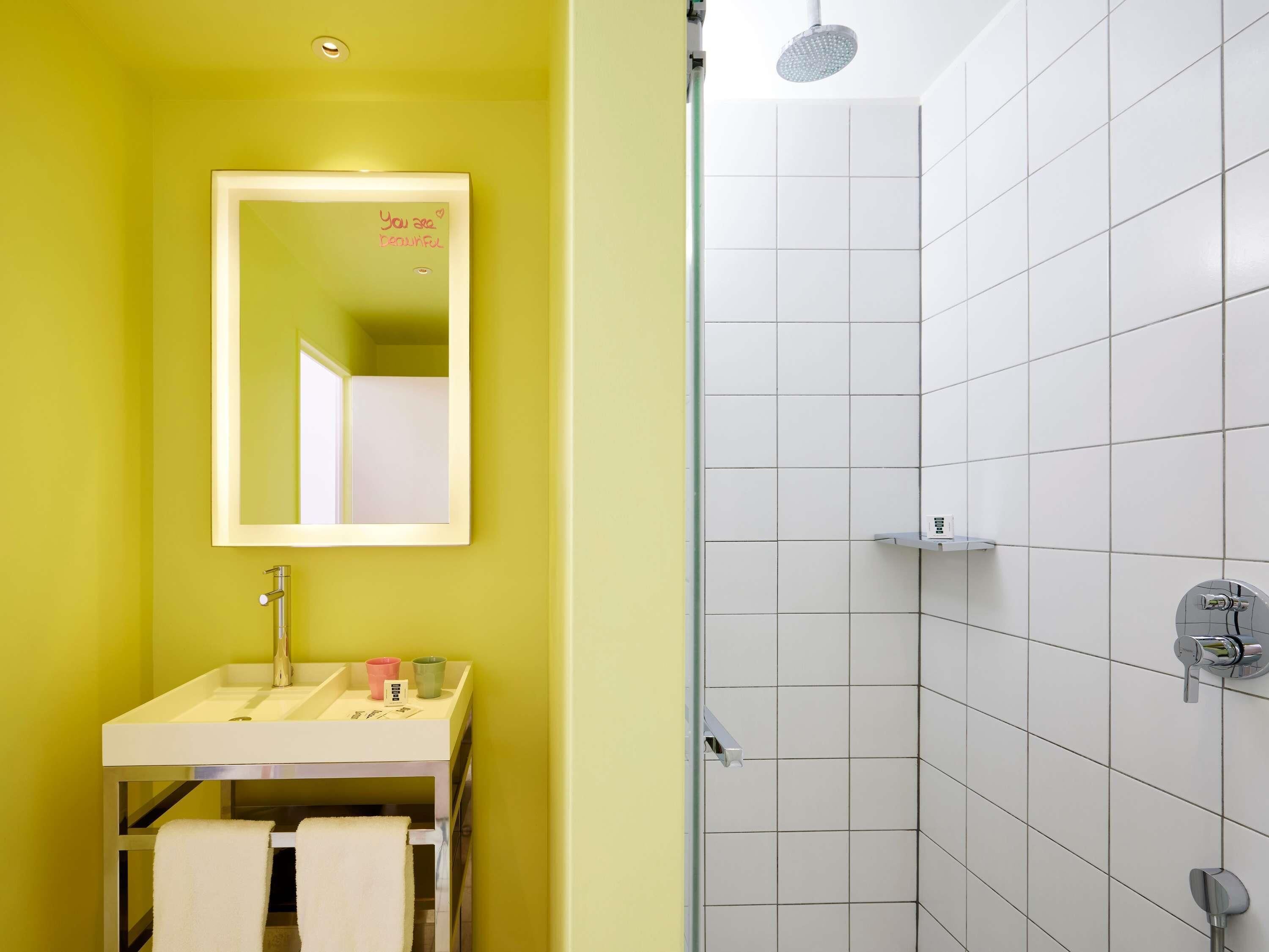 A bathroom with a yellow wall, a white sink, a mirror, and a shower area.