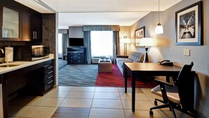 A modern hotel room with a kitchen area, a dining table with a chair, a sofa, a TV, and a large window with curtains. - Homewood Suites by Hilton DuBois, PA (DuBois)
