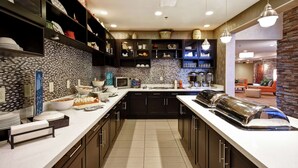 A modern kitchen with dark cabinetry, white countertops, and a tiled backsplash. There are built-in shelves with dishes and a microwave on the counter. - Homewood Suites by Hilton DuBois, PA (DuBois)