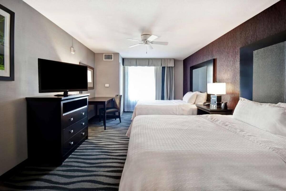 A hotel room with two beds, a TV, a desk, and a ceiling fan.