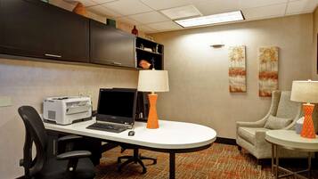 A hotel room with a desk, office chair, printer, laptop, lamp, and a sofa.