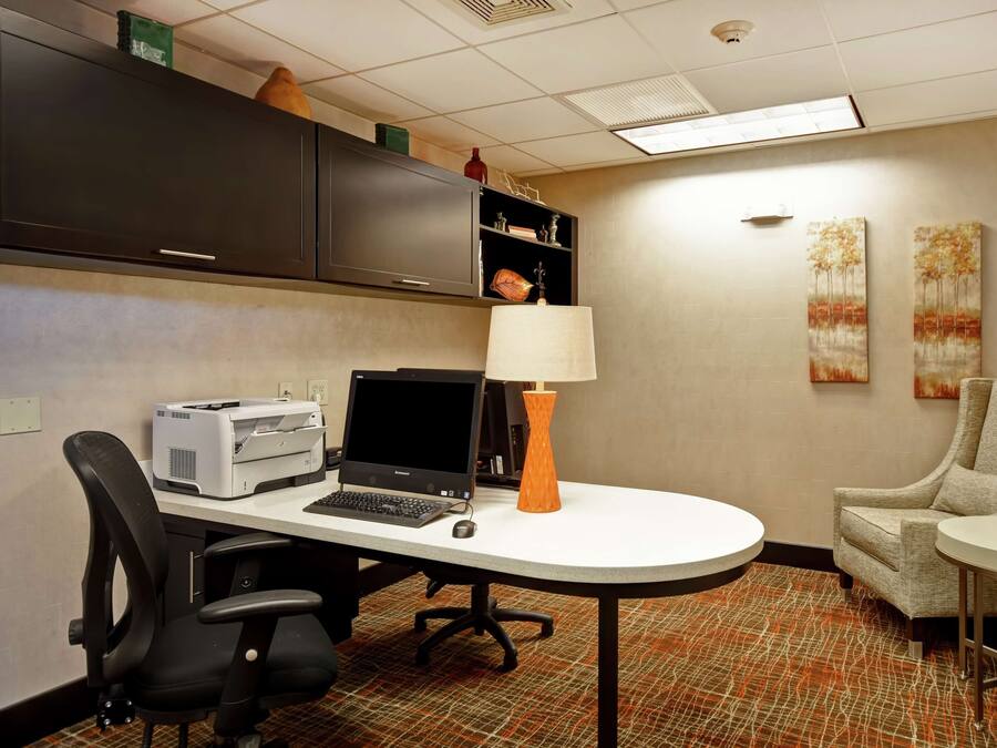 A hotel room with a desk, office chair, printer, laptop, lamp, and a sofa.