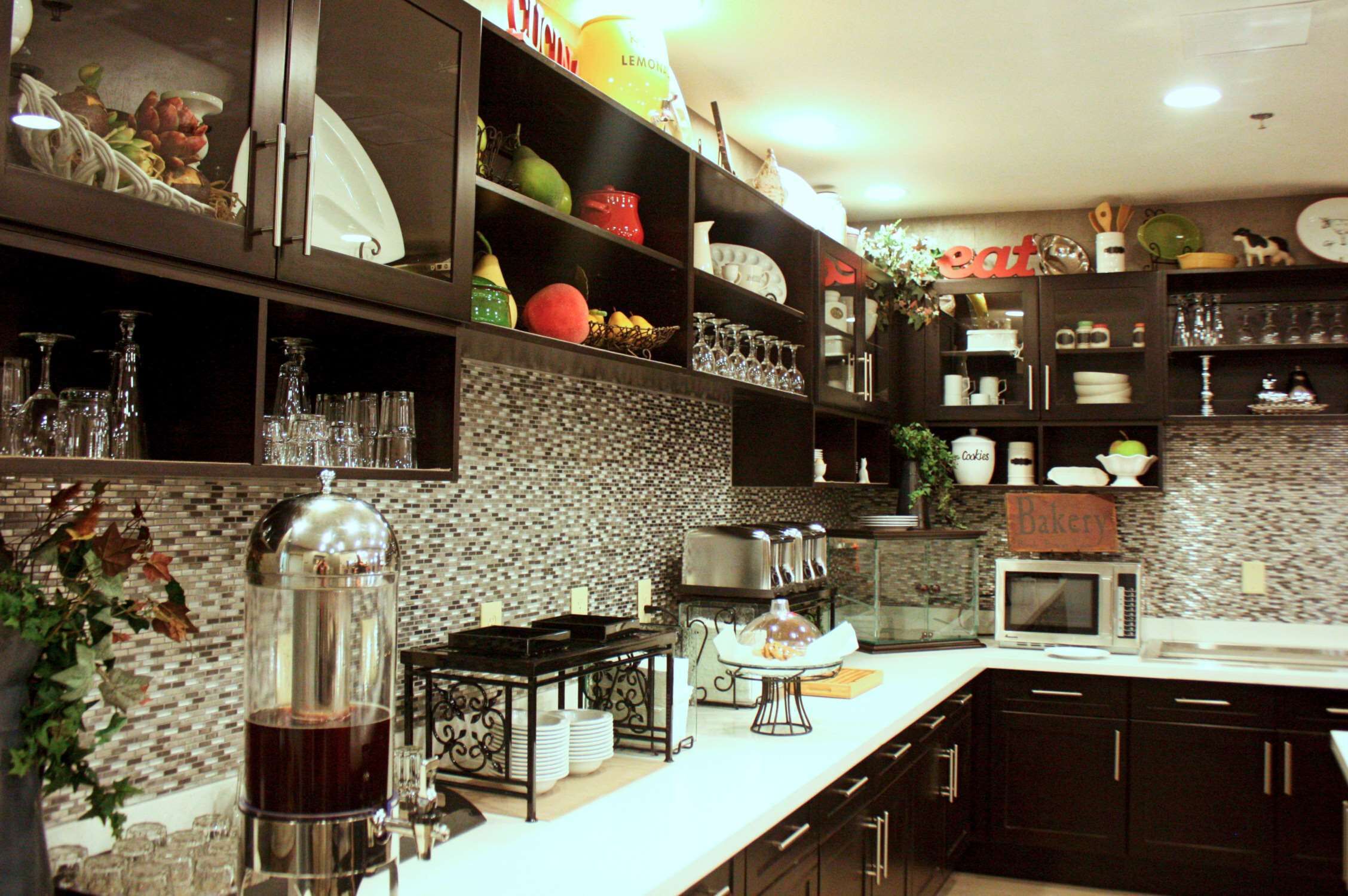 A modern kitchen with dark cabinetry, a tiled backsplash, and various kitchen appliances.