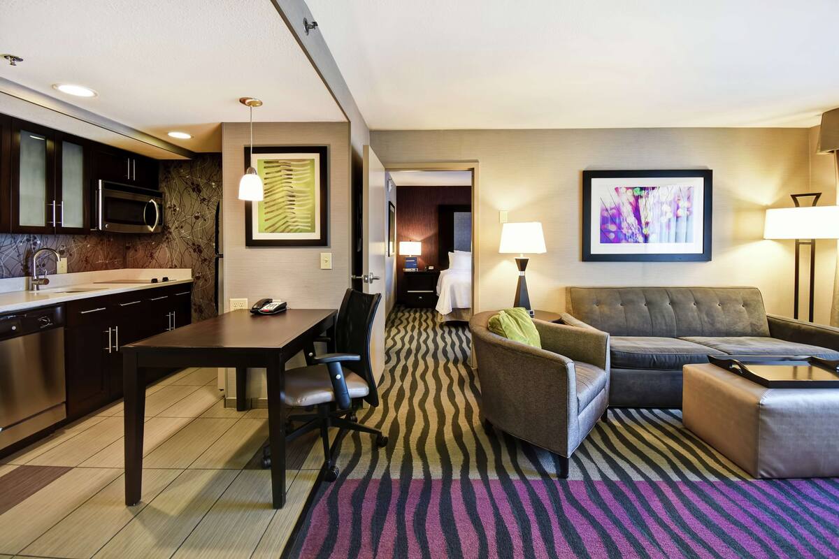 A hotel room with a kitchenette, a dining area, a sofa, and a bed.