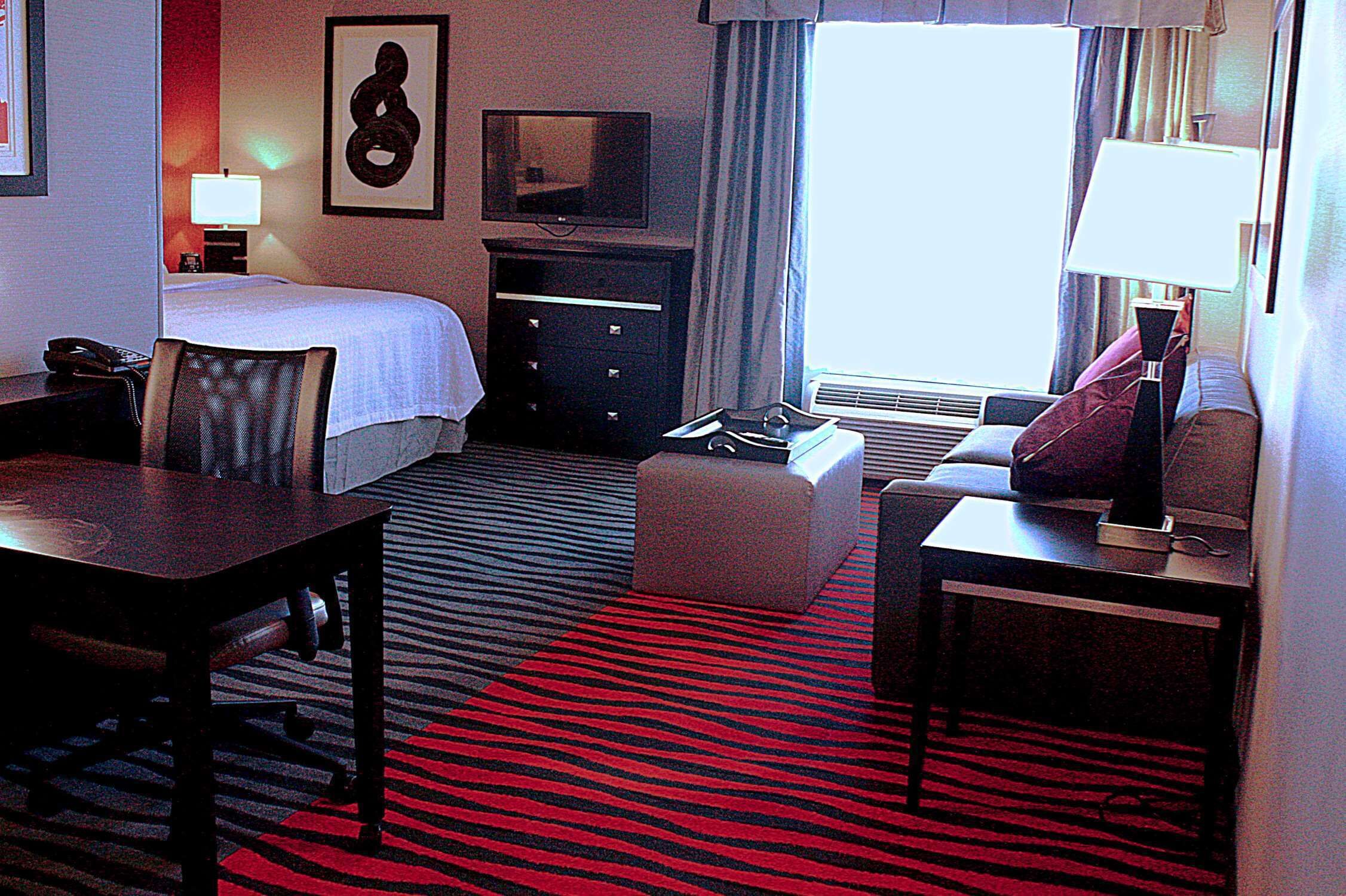 Une chambre d’hôtel équipée d’un lit, d’un bureau, d’une chaise, d’une télévision, d’une lampe et d’une fenêtre avec des rideaux.