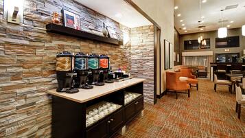 Um saguão de hotel com parede de pedra, um espaço para café, área de estar e um balcão de recepção.