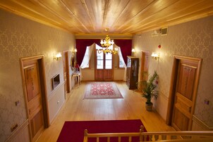 Un pasillo con pisos de madera, una alfombra roja y un candelabro. Hay dos puertas a cada lado, una de ellas con la etiqueta 'Premium'.