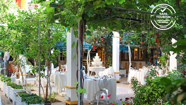 An outdoor restaurant with white tables and chairs, surrounded by potted plants and flowers.