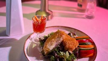 Une assiette de nourriture avec une salade, un petit verre d’une boisson rouge, une bouteille et une plante en pot, le tout posé sur une table.