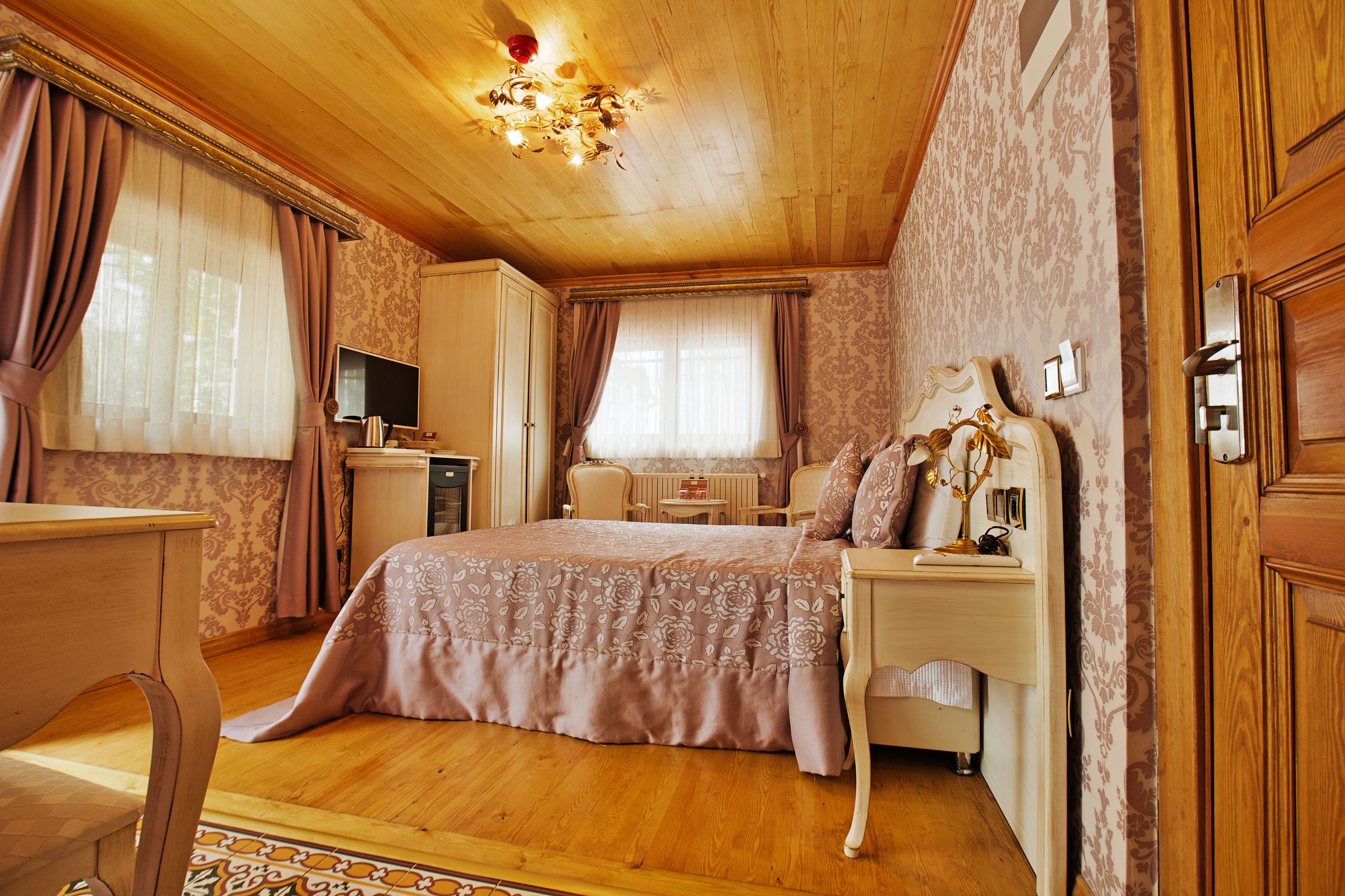 Un dormitorio con techo de madera, una cama con colcha estampada, una mesita de noche con lámpara y un televisor sobre un mueble.