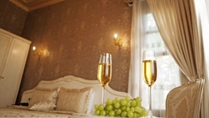 A bedroom with a bed, two glasses of champagne, and a bowl of grapes.
