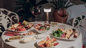 A round table with various dishes, two glasses of red wine, and a white lamp.