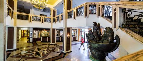 A spacious lobby with a geometric patterned floor, a grand chandelier, and a statue of a figure in a boat.