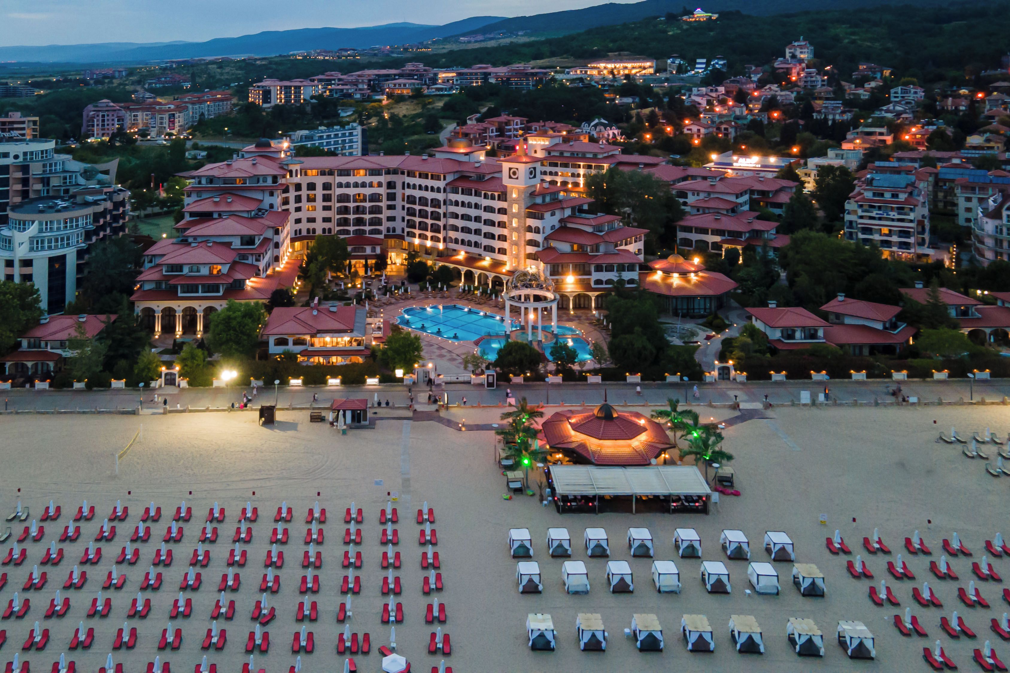A resort with multiple buildings, a swimming pool, and a beach area with sun loungers.