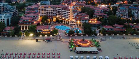 A resort with multiple buildings, a swimming pool, and a beach area with sun loungers.