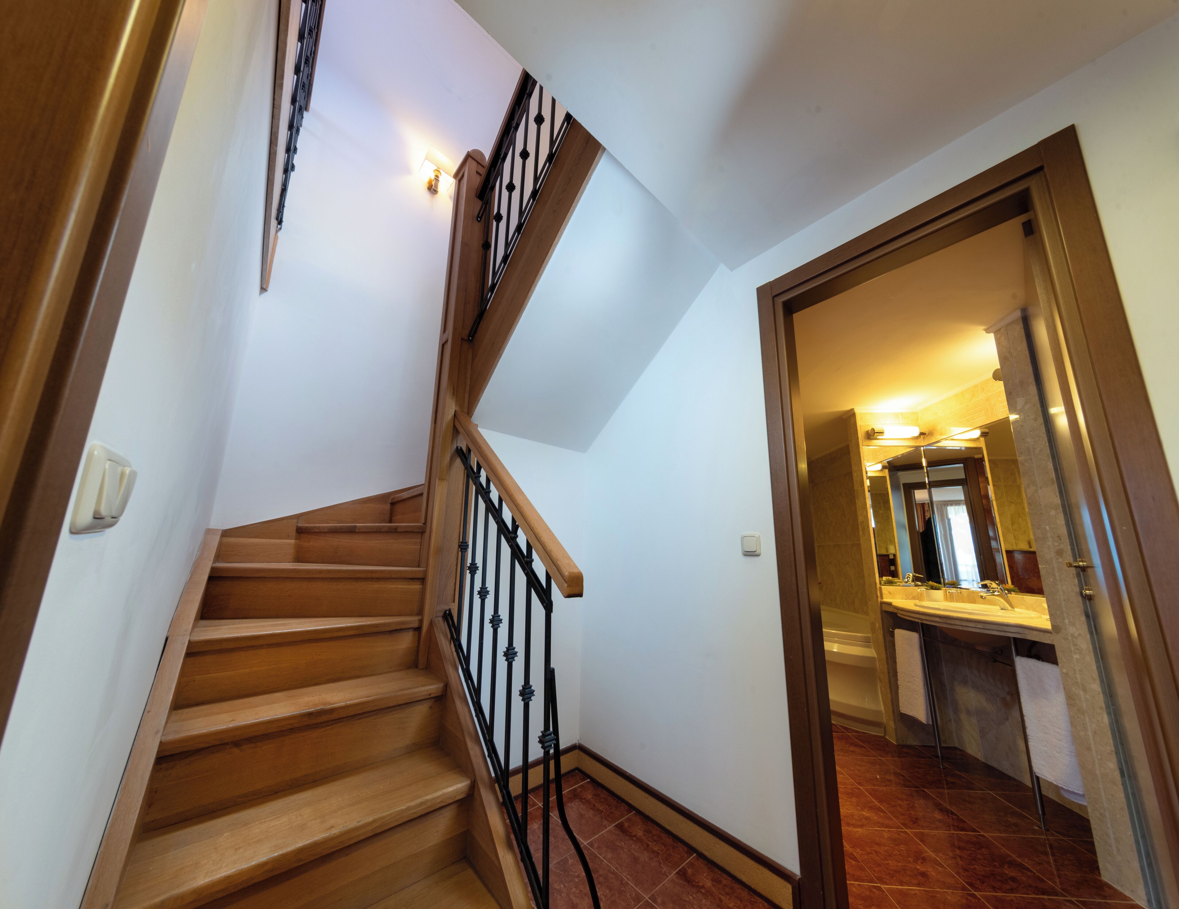 A wooden staircase with black railings leading to a bathroom with a sink and mirror.