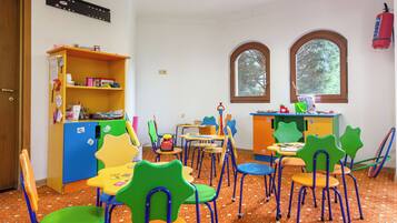 A children's playroom with colorful chairs, tables, and a bookshelf.