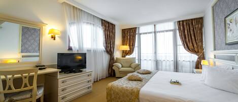 A hotel room with a bed, a desk with a television, a chair, and a dresser.