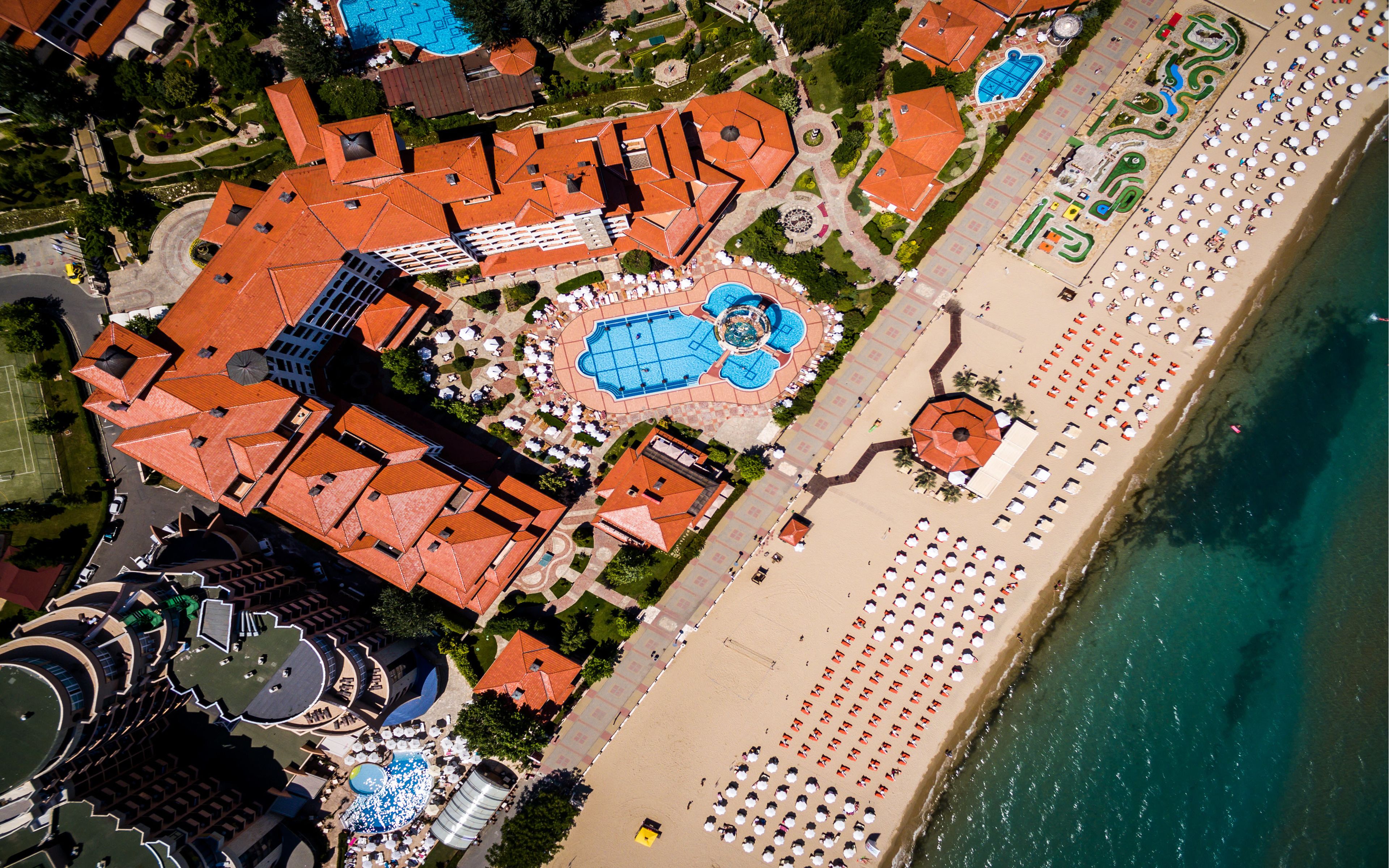 An aerial view of a resort with multiple buildings, a large pool area, and a beach with sun loungers.