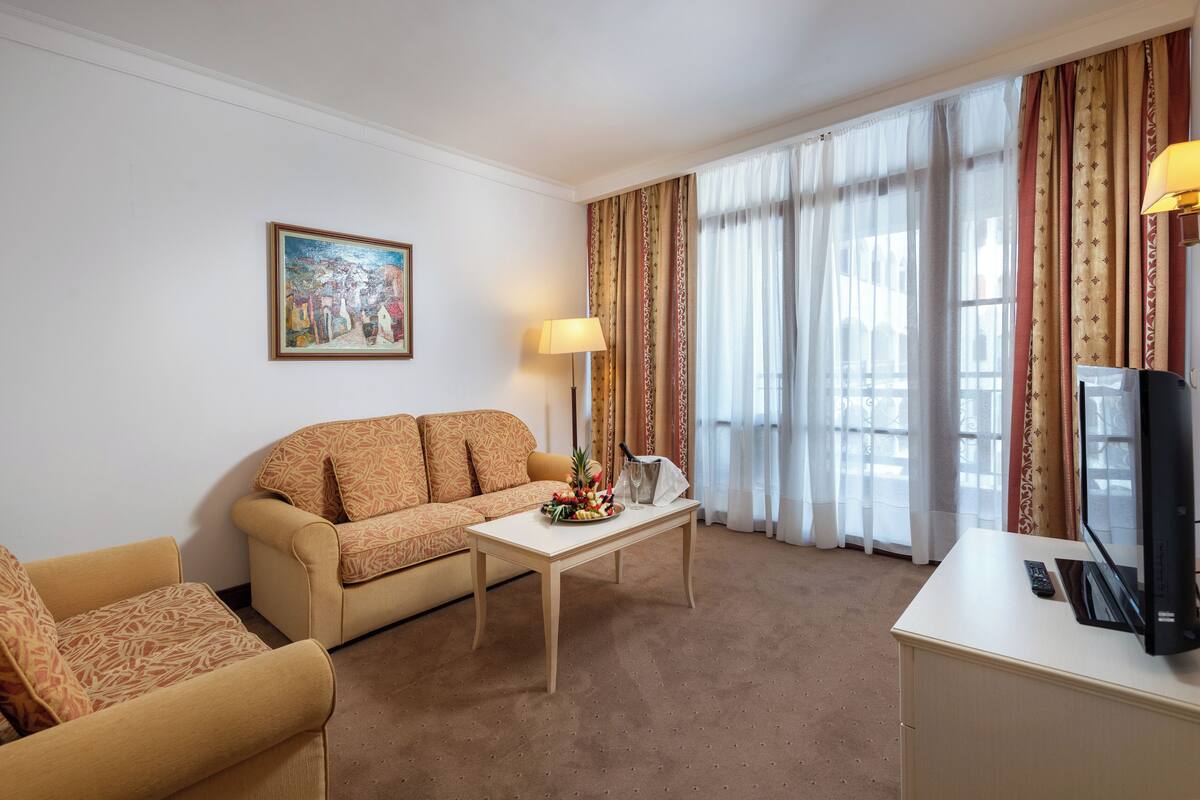 Habitación de hotel con un sofá color crema, una mesita con fruteros, un televisor y una lámpara.