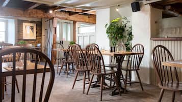 A rustic dining area with wooden tables and chairs, stone walls, and a large potted plant.