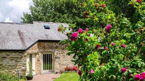 A stone building with a green door, surrounded by lush greenery and vibrant flowers. - The Plume of Feathers (Newquay)