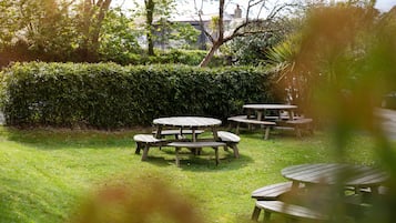 A garden with wooden picnic tables and a hedge.