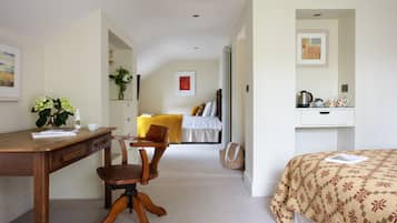 Habitación de hotel con un escritorio de madera, una silla, una cama con colcha estampada, una mesita de noche con hervidor y un cuadro en la pared.
