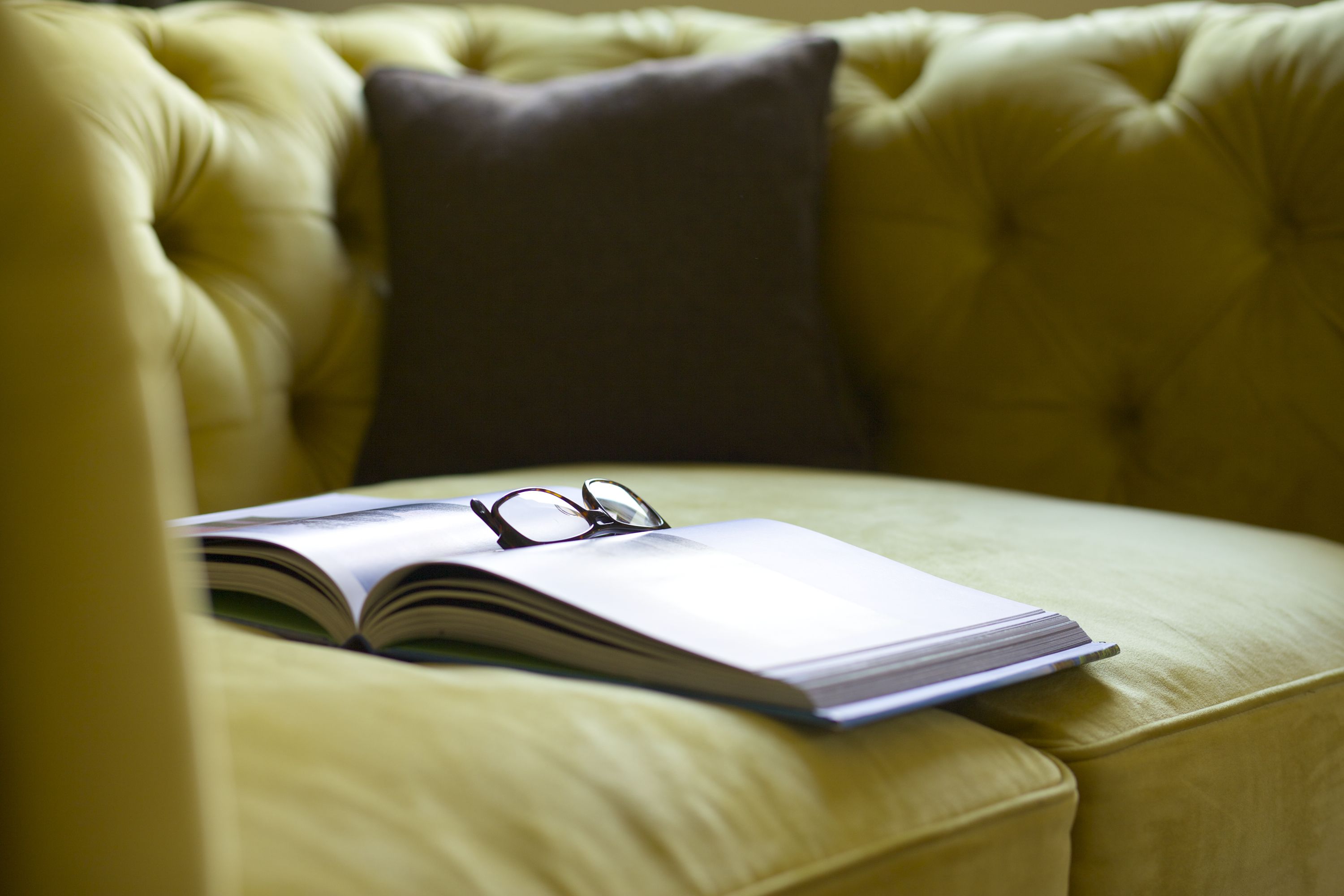 A yellow sofa with a book and glasses on it.