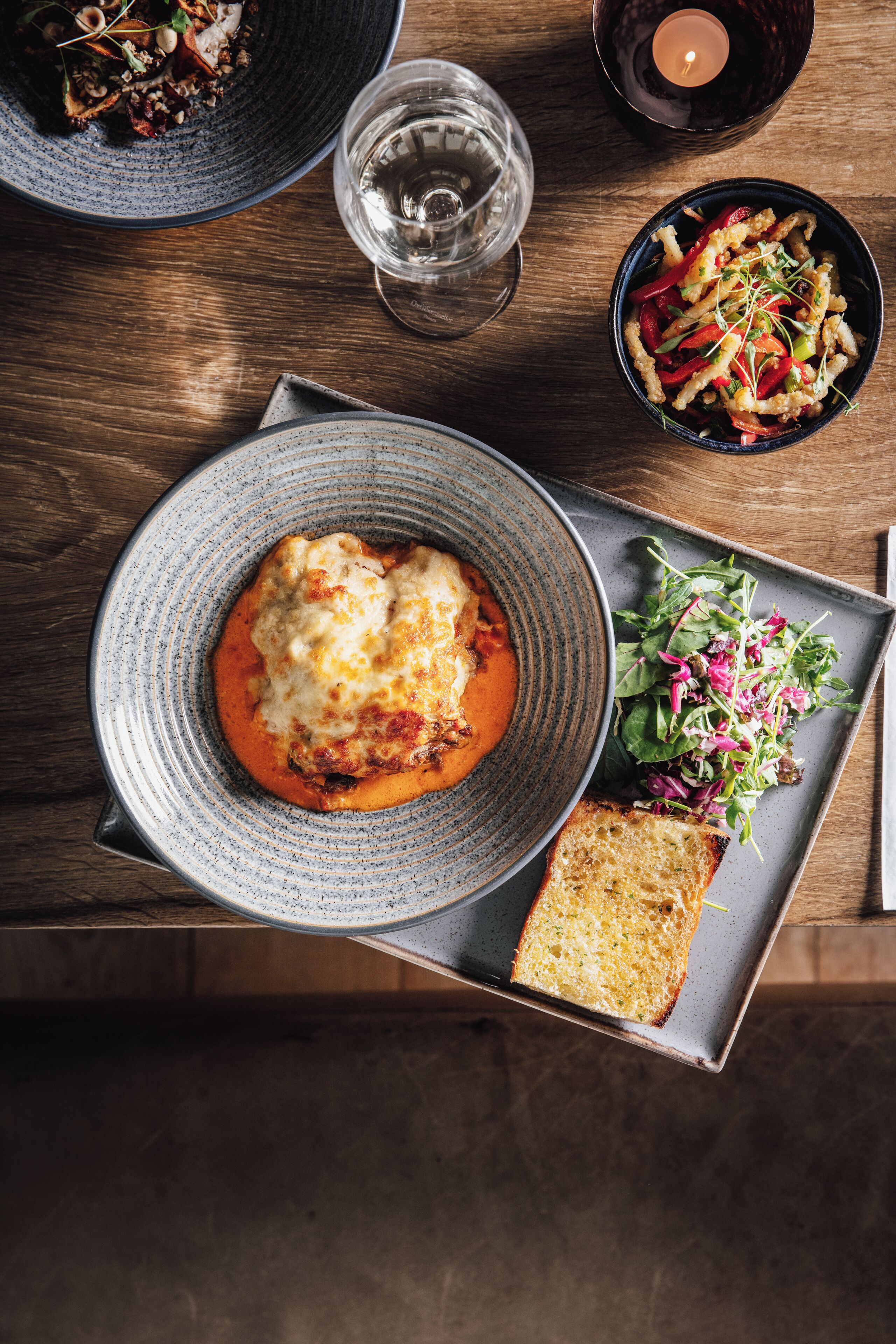 A dining table with a plate of food, a glass of water, and a candle.