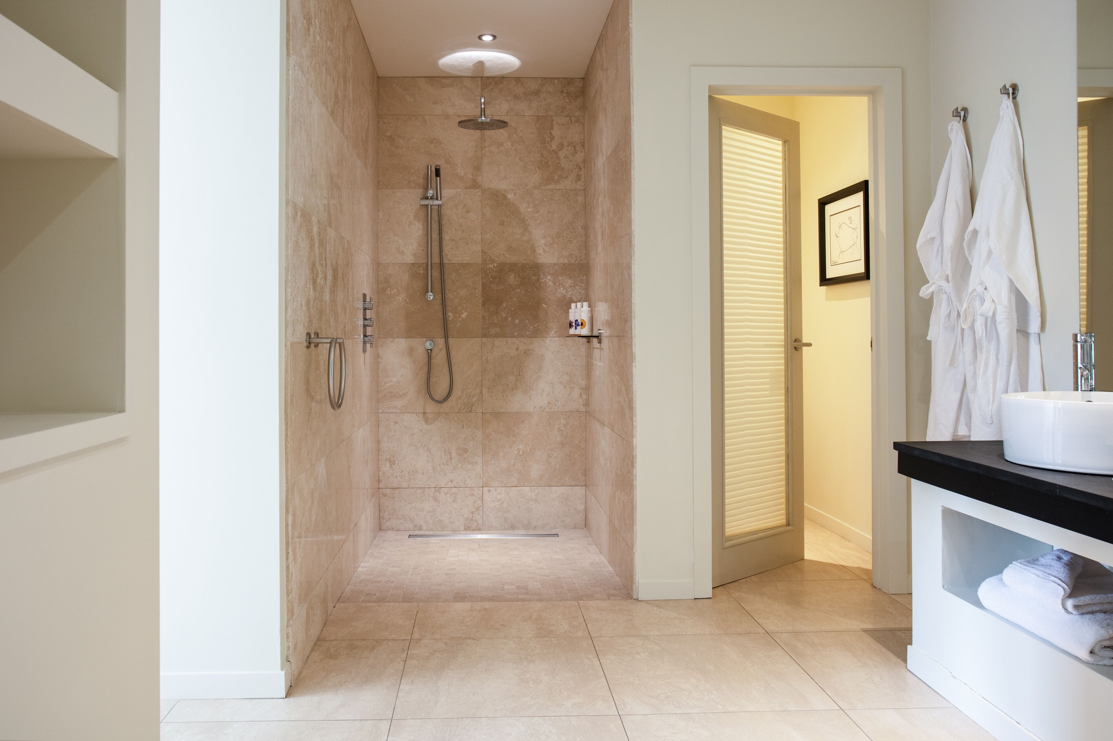 Un baño moderno con cabina de ducha, tocador con lavabo y toallas colgadas en un perchero.