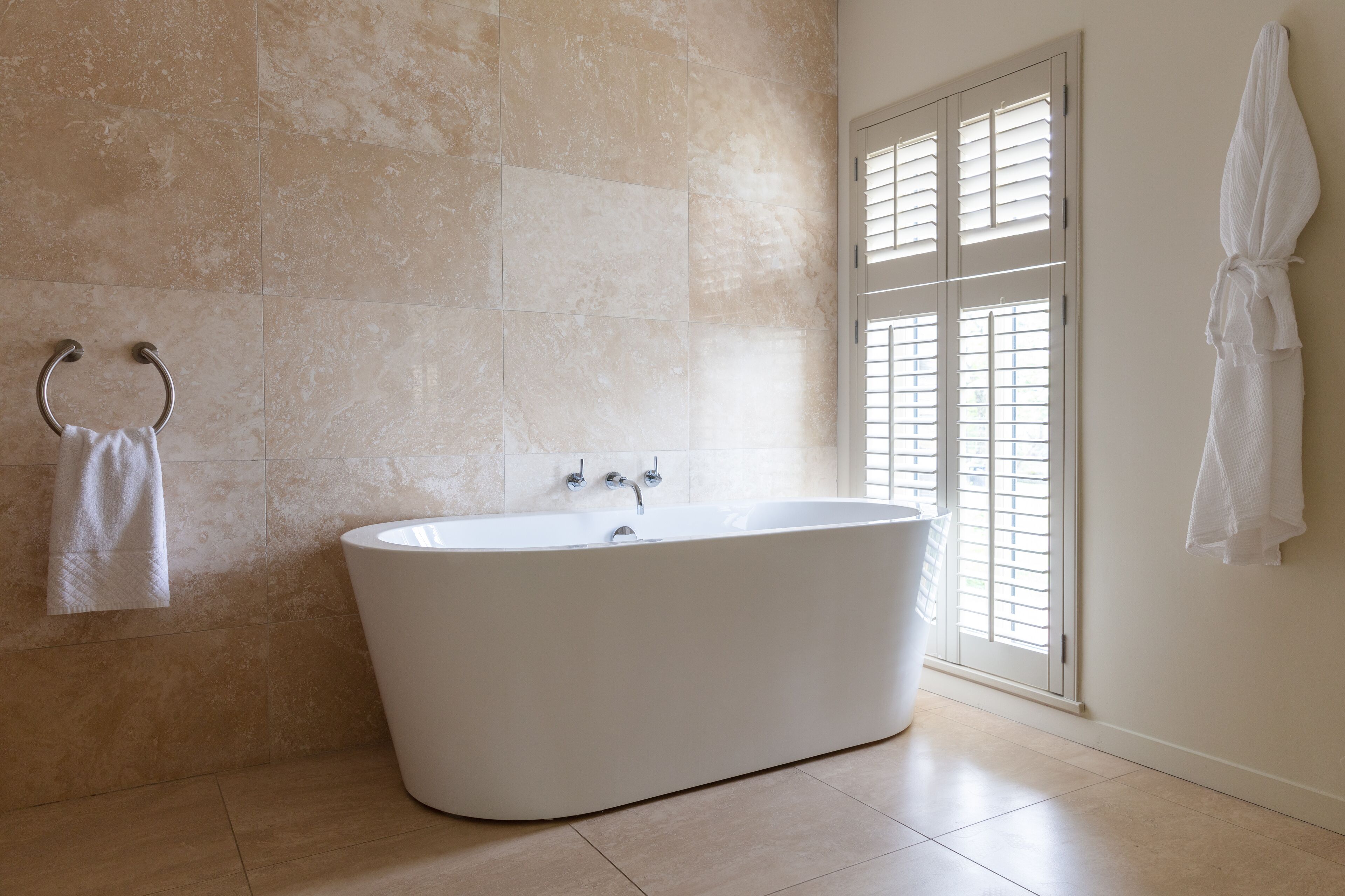 A modern bathroom with a freestanding bathtub, a towel rack, and a window with blinds.