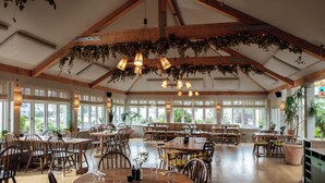 A spacious restaurant with wooden tables and chairs, large windows, and hanging plants. - The Plume of Feathers (Newquay)