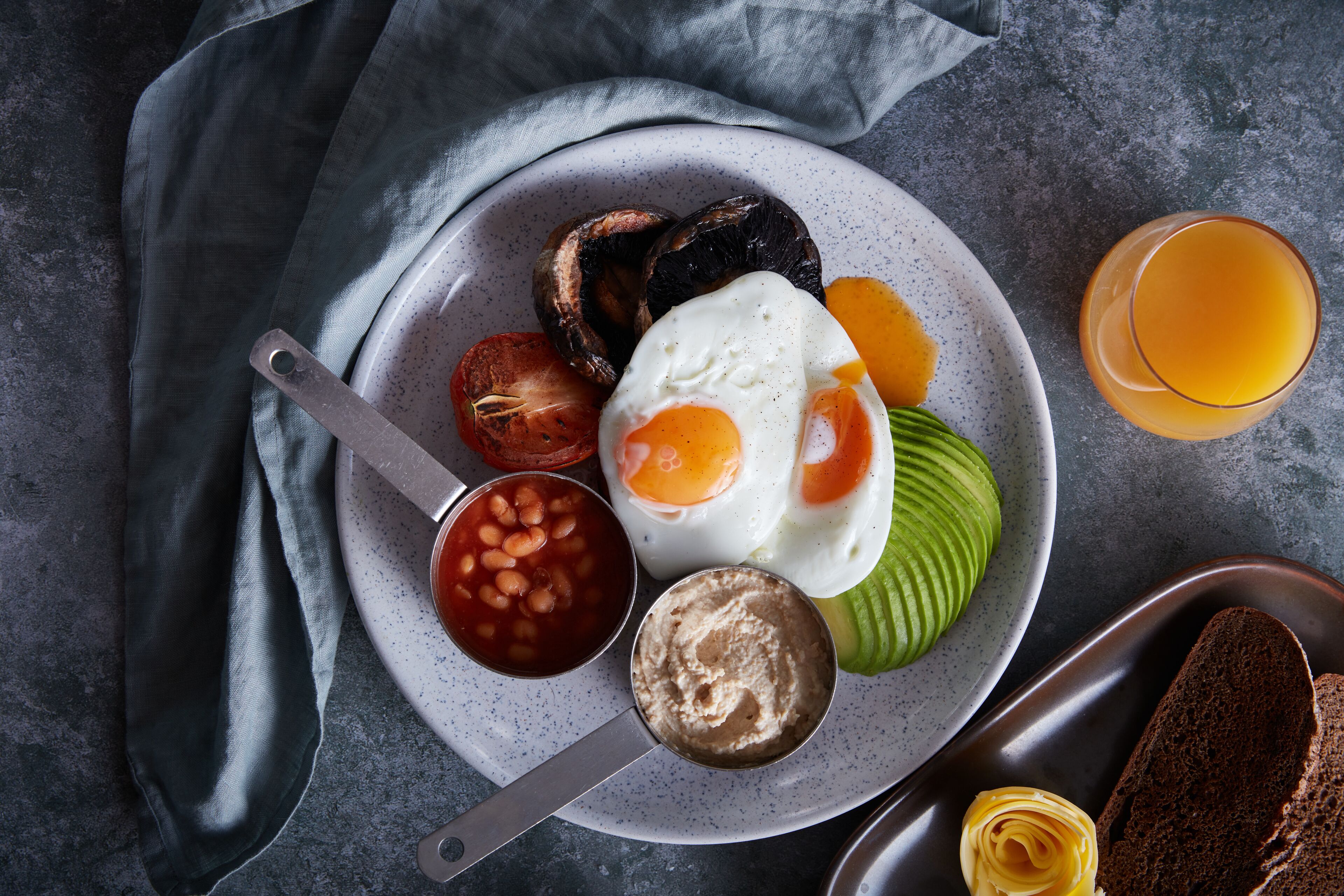 A plate with eggs, beans, avocado, and toast on a gray surface.