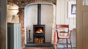 A cozy room with a fireplace, a chair, and a desk with a lamp. - The Plume of Feathers (Newquay)