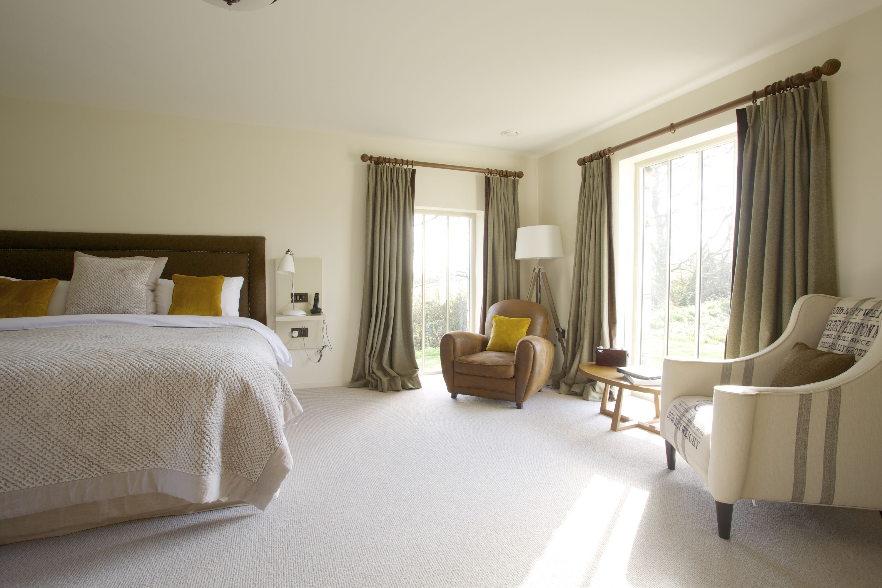 A hotel room with a large bed, a chair, a lamp, and curtains.