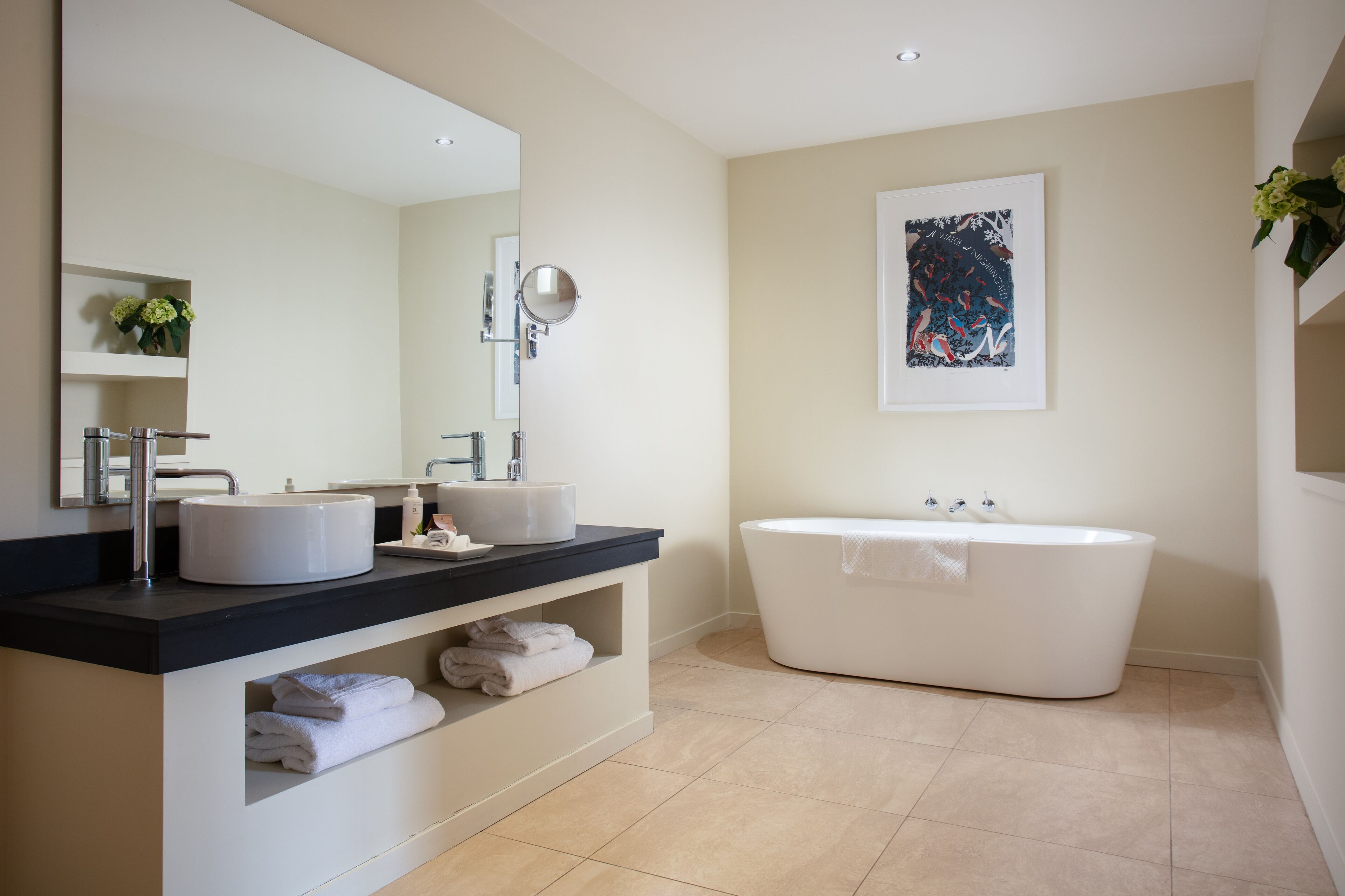 A modern bathroom with two sinks, a large mirror, a bathtub, and a framed artwork on the wall.